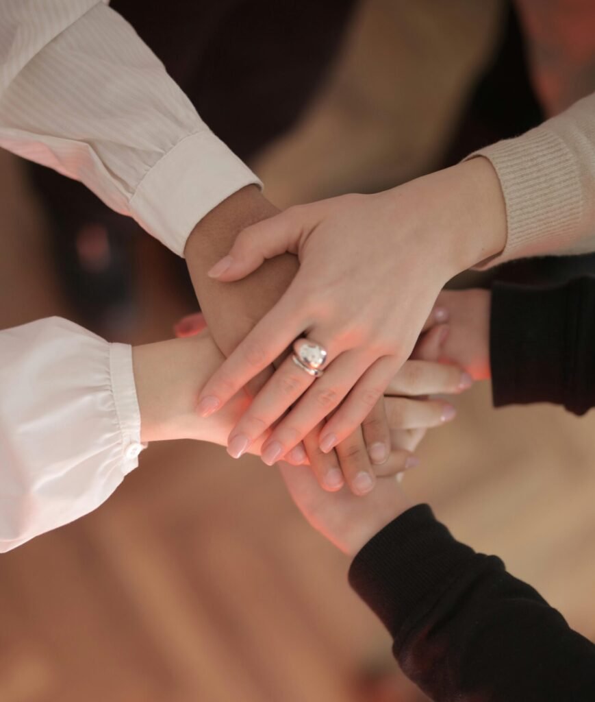 Top view of faceless friends in different clothes stacking hands together while standing on wooden floor indoor on sunny day